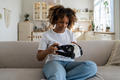 Curious African American woman sitting on couch holding VR headset - PhotoDune Item for Sale