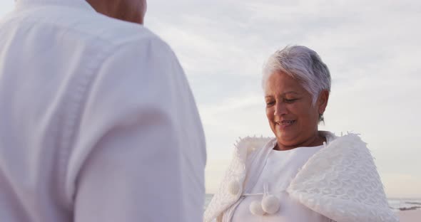 Happy hispanic senior woman taking a vow to man on beach at sunset