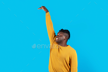ible Object With Hand While Standing Isolated Over Blue Studio Background, Young Black Man Looking Up And Checking Hight, Copy Space