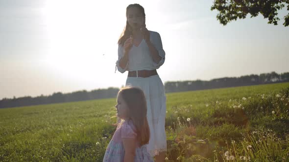 Mom in a White Dress Blows Soap Bubbles for Her Little Daughter