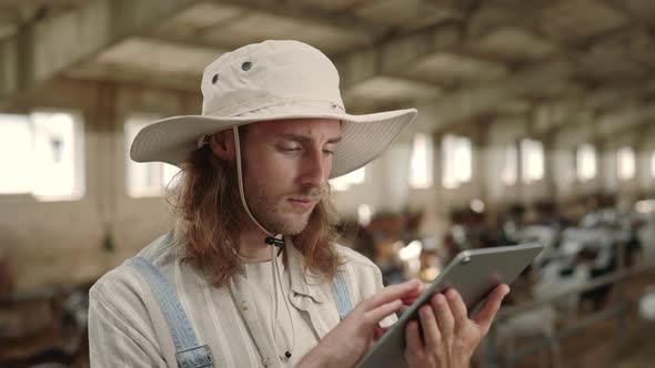 Farmer Standing at Ranch with Goats and Working on Tablet