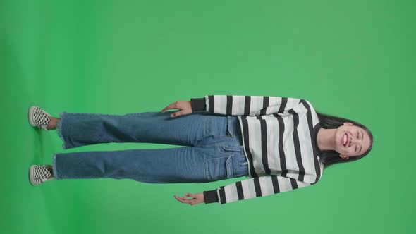 Full Body Of A Smiling Asian Woman Dabbing While Standing In Front Of Green Screen Background