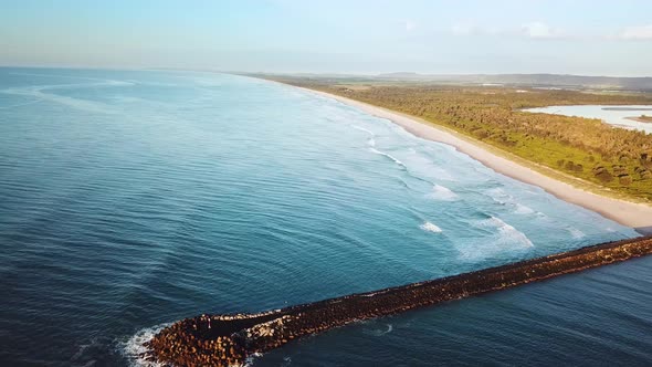 Drone moving side-on showing long straight beach and man made rock wall. Ballina, Australia.