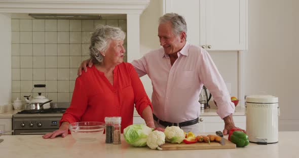 Portrait of caucasian senior couple embracing each other in the kitchen at home