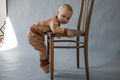 The kid hangs on a wooden chair, trying to climb on it - PhotoDune Item for Sale