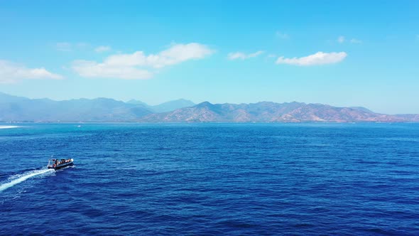 Boat sailing through blue sea toward beautiful mountain islands on a bright blue sky with clouds bac