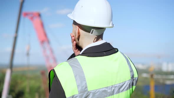 Back View Thoughtful Caucasian Foreman Standing at Industrial Park with Tower Crane Looking Away