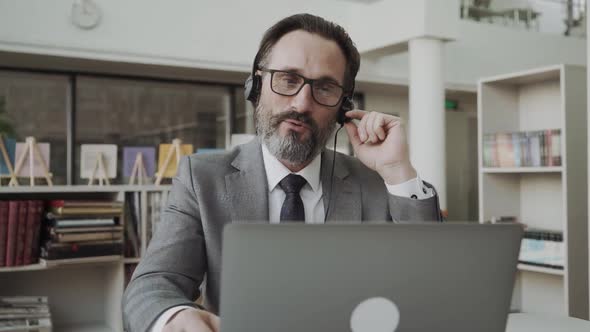 Middleaged Businessman Manager Wearing Earphones Holding Video Call Looking at Laptop Screen