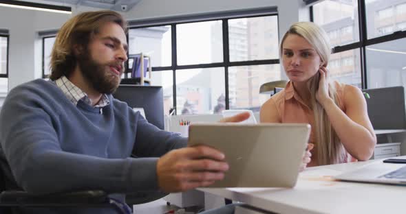 Disabled caucasian businessman sitting on wheelchair using digital tablet talking to coworker in off