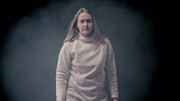 Fencing Training - Young Woman Fencer with Long Hair Walking Out From the Dark - Gets Into Position