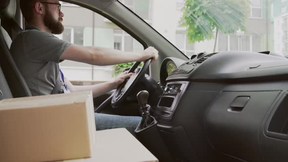 Young Delivery Man Driving Car with Parcels on Front Seat