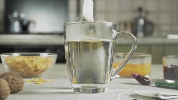 Tea bag falls into a cup of hot water on a table prepared for breakfast