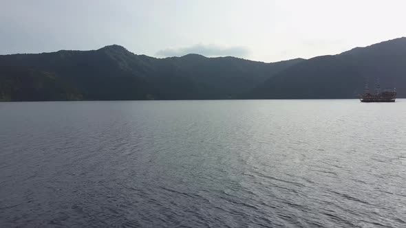 Backwards close flight over the water on lake ashi in hakone with ship