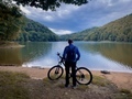 Rear view of fit man and his bike standing near a lake surrounded by green forest on a cloudy day - PhotoDune Item for Sale