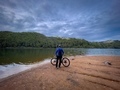 Rear view of fit man and his bike standing near a lake surrounded by green forest on a cloudy day - PhotoDune Item for Sale