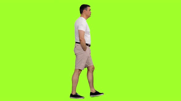 A Man in White T-shirt and Shorts Walks on Green Background