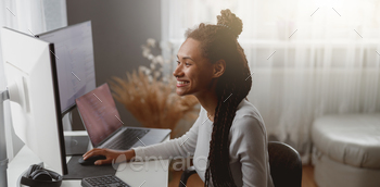 Smiled cheerful female web expert sitting at desk in living room coding on computer