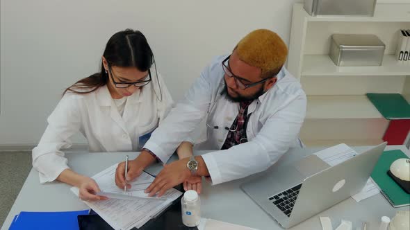 Male Doctor Showing His Unexperienced Female Trainee How To Fill in Forms