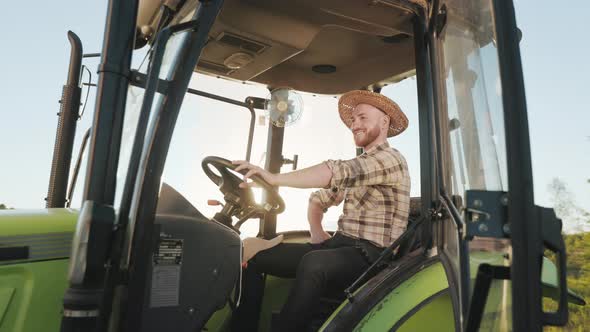 A Young Farmer is Sitting at the Wheel of a Tractor