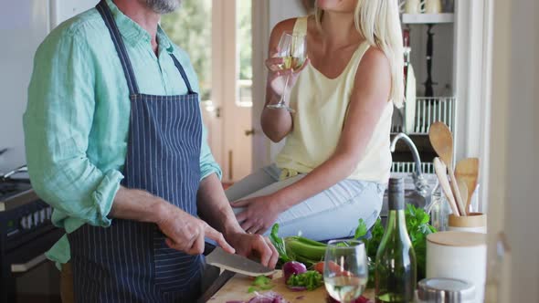 Happy caucasian mature couple cooking together and drinking wine in the kitchen