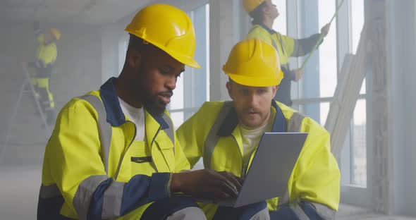 Portrait of Two Diverse Builders Reading Plan of Building on Laptop