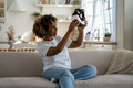 Excited Black woman sitting on sofa at home holding VR glasses. First experience of virtual reality. - PhotoDune Item for Sale