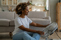 Satisfied happy young black woman sitting on floor in front of electrical fan cooling down at home - PhotoDune Item for Sale