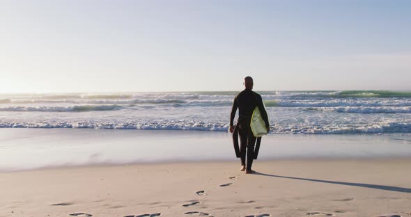 Senior african american man walking with a surfboard at the beach