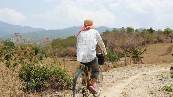 Young Woman Farmer In A Straw Hat Rides A Bicycle On the Countryside Road.  Footage. 