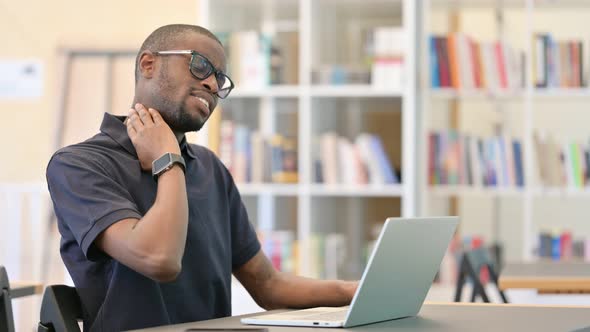 Hardworking Young African Man with Laptop Having Neck Pain in Library
