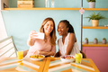 Two young women, caucasian and black one, taking selfie with mobile phone in the cafe - PhotoDune Item for Sale