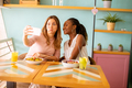 Two young women, caucasian and black one, taking selfie with mobile phone in the cafe - PhotoDune Item for Sale