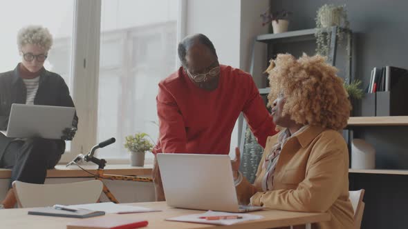 Black Man and Woman Speaking and Using Laptop in Office