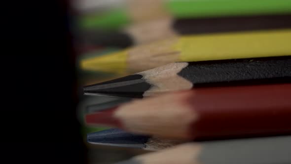 Many Colored Pencils Lie in a Row on a Black Background. The Camera Moves Forward or Dolly In.