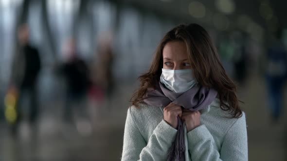 Woman with Face Mask Is Standing in Pedestrian Tunnel of Subway or Mall and Wrapping in Coat