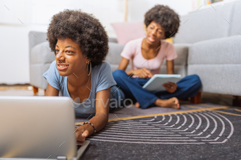 Twins with afro hairstyle, doing a homework on the laptop and digital tablet, sitting on the rug