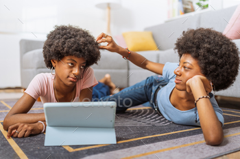 Black twin sisters, using the digital tablet and one touching the other's hair