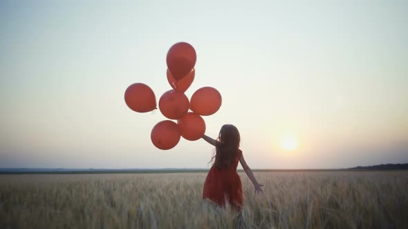 Happy Young Girl with Balloons Running in the Wheat Field at Sunset.  Video.