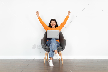 ual outfit businesswoman siting in armchair with laptop on her lap, gesturing and smiling, white wall background, business success, copy space