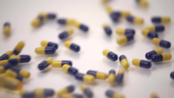Slow Motion Macro of Blue and Yellow Pills Pushing One Yellow Pill Out of Frame on White Background
