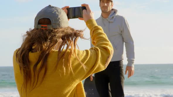 Rear view of young caucasian woman clicking photo of young caucasian man with camera on the beach 4k