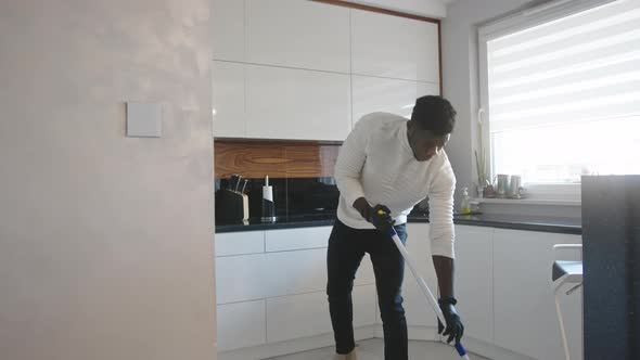 Handsome Black Man Dancing and Singing While Cleaning Floor in the Kitchen. Domestic Life Concept