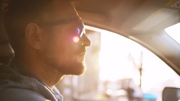 Handsome Man with Beard in Mirror Sunglasses Driving Car in City with Sunflare