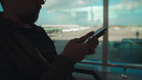 Man Is Swiping on Sensor Screen of Mobile Phone Sitting in Airport, Close-up