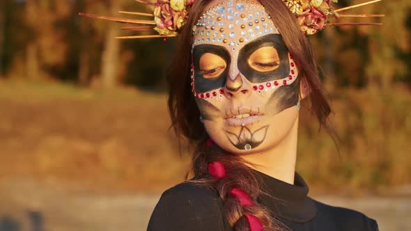 A Young Woman with Santa Muerte Makeup Dressed in a Black Dress of Death Walks Against the Backdrop