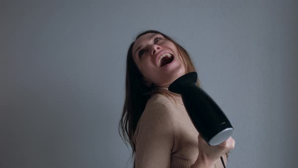 Beautiful Young Woman Singing While Using Hairdryer