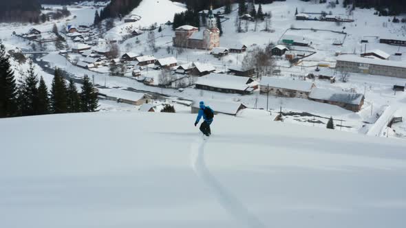 Aerial View of a Snowboard That Slides Down a Mountain Against the Background of a Village