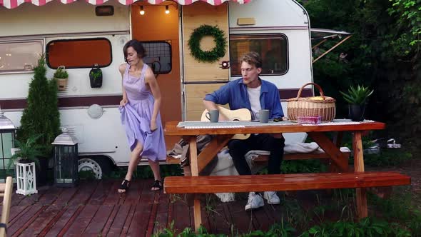 Brunette Girl in Blue Summer Dress Girl Dancing While Man Playing Guitar Sitting at the Wooden Table