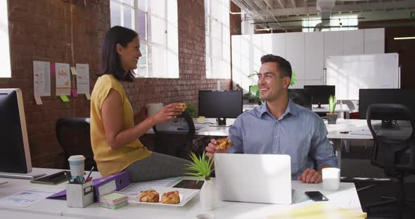 Diverse male and female business colleagues eating pastries and smiling