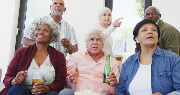 Happy senior diverse people watching tv with beer at retirement home